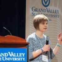 Student presenting with a gestured hand, standing to the side of a GVSU podium